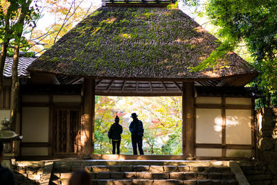 People standing by building against trees