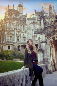 Smiling woman sitting on concrete wall against historic building