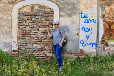 Portrait of woman standing against brick wall by text