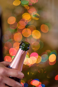 Closeup of hand holding champagne bottle on new years eve with holiday lights bokeh in background