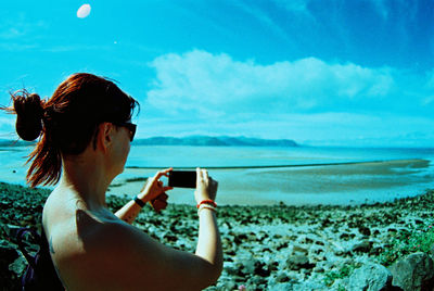 Woman photographing at beach against sky