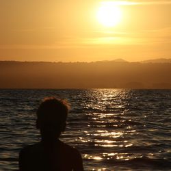 Rear view of silhouette woman looking at sea against sky during sunset