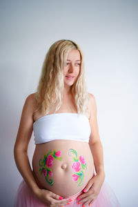 The belly of a pregnant blonde woman on a light background, the girl put her hand on her stomach.