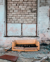 Abandoned sofa against brick wall of old building