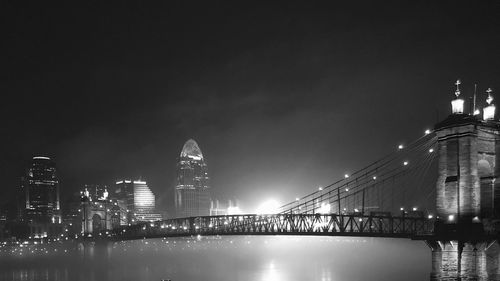 Illuminated bridge over river and buildings in city at night