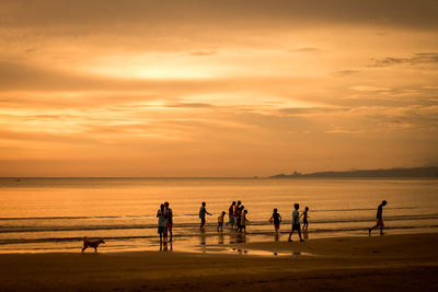 People playing on beach against sky during sunset