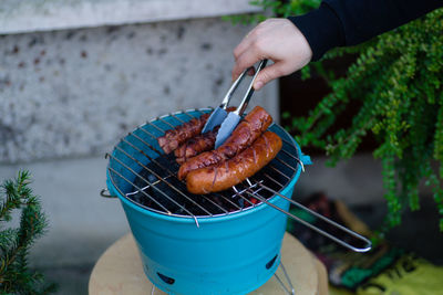 Cropped hand preparing sausages on barbecue grill