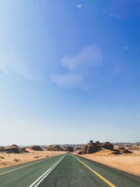 Road passing through desert against blue sky