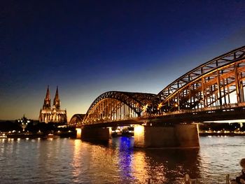 Illuminated bridge over river against sky in city