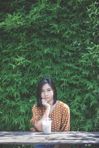 Portrait of woman sitting with drink on table against plants