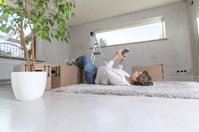 Young woman using digital tablet while lying on carpet at home