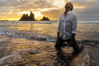 Scenic view of man in sea against cloudy sky at sunset