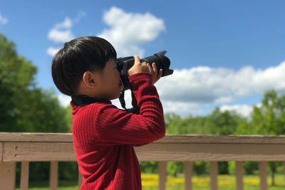 Side view of boy standing by railing against sky