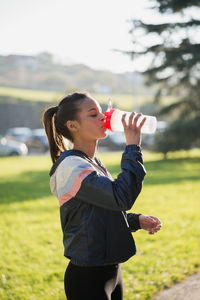 Portrait of young woman drinking water while standing outdoors