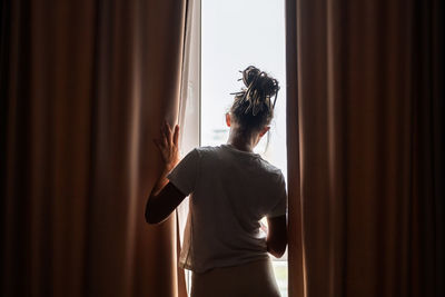 Woman opening curtains in sunlit room. concept of morning routine.