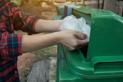 Cropped hands of woman putting garbage in can