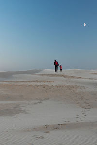 Rear view of man and child walking hand in hand on sand dunes at sunest