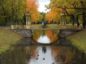 Couple standing on footbridge over lake in park during autumn