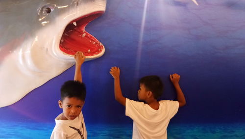 Cheerful boys playing with shark sculpture on wall