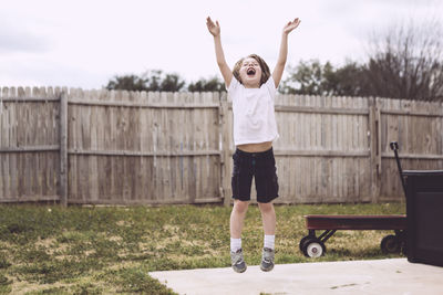 Front view of young boy jumping into the air in backyard