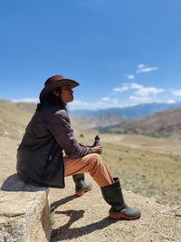 Side view of man sitting on land against sky