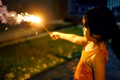 Girl holding illuminated sparkler at night