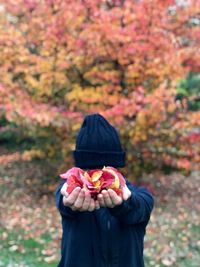 Person holding dry leaves in front of face while standing against trees