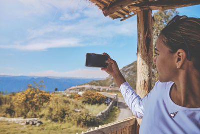 Side view of young woman photographing against sky