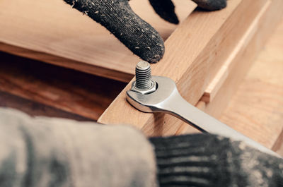 Male hands tighten nut on thread of bolt screwed into wooden structure.