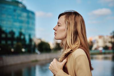 Side view of woman looking at camera against sky