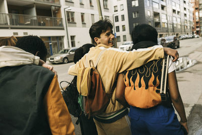 Happy young man with arms around friends while walking on sidewalk