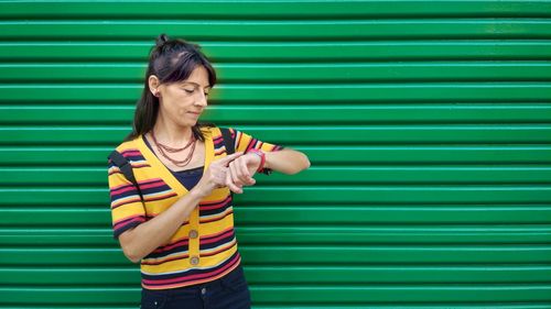 Smiling mature woman checking time against green 