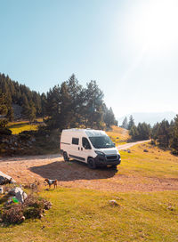 Scenic view of green slope near hill with lush forest and parked white van on roadway in sunny day in catalonia