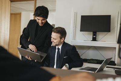 Smiling businessman explaining male colleague over laptop at office