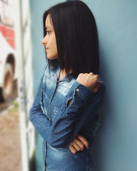 Young woman looking away while leaning on wall