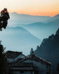 House amidst trees and mountains against sky during sunset