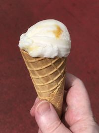 Close-up of hand holding ice cream cone against wall