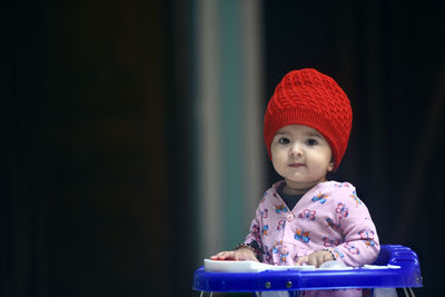 Indian baby girl wearing pink  jacket and woolen cap siting on a walker and giving cute expressions