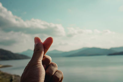 Cropped hand snapping fingers against sky