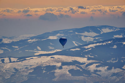 Aerial view of hot air balloon flying over mountains against sky