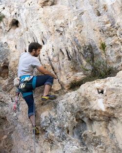 Boy doing sport climbing on the mountain with rope and carabiners