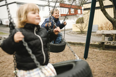 Playful brother and sister having fun on tire swing at park