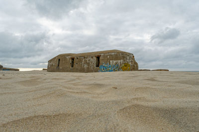 Stone structure on beach against cloudy sky