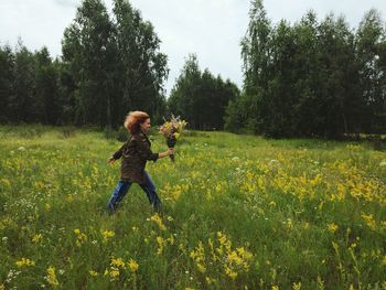 Side view of young woman with flowers walking on grassy field against sky