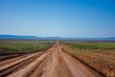 Dirt road passing through landscape against sky