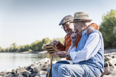 Two old friends sitting by the riverside, using digital tablet