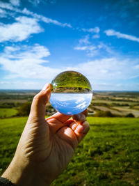 Cropped hand holding crystal ball against landscape