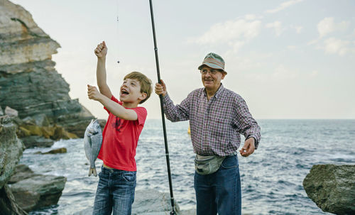 Happy boy holding fish on fishing line caught by his grandfather