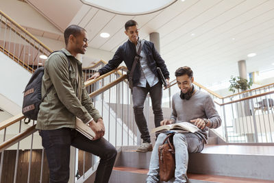 Smiling male friends discussing over book on steps in university