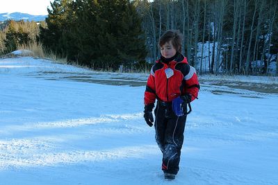 Full length of sad boy wearing warm clothing while walking on snow during winter